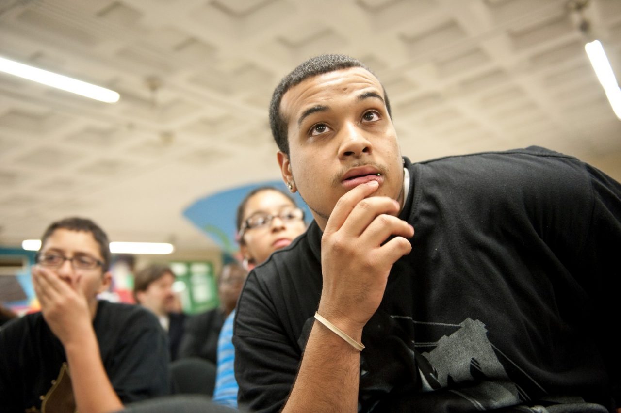 Young men listen to a speaker at a meeting.