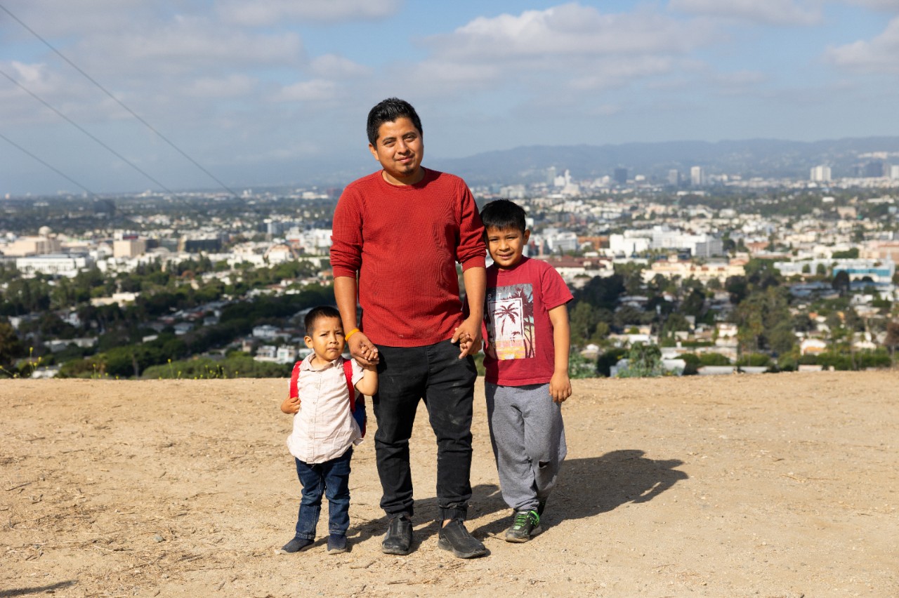 A man holding hands with his children at the top of a scenic overlook.