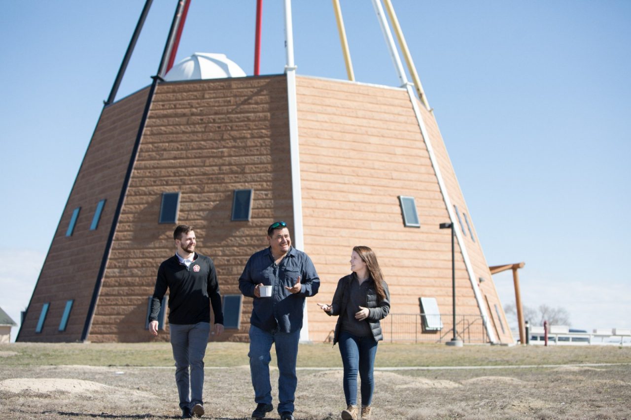 Three people walking away from a large, teepee-shaped brick building.