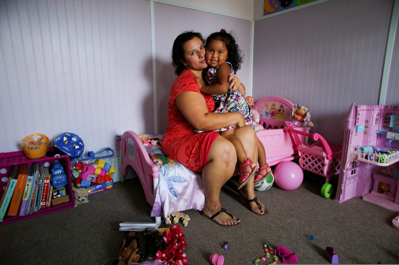 A mother and daughter sit together amidst toys and books.
