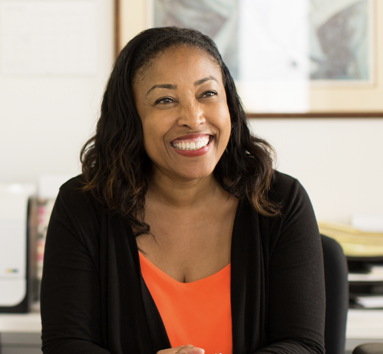 A happy woman sits behind her desk with a computer monitor in the background.