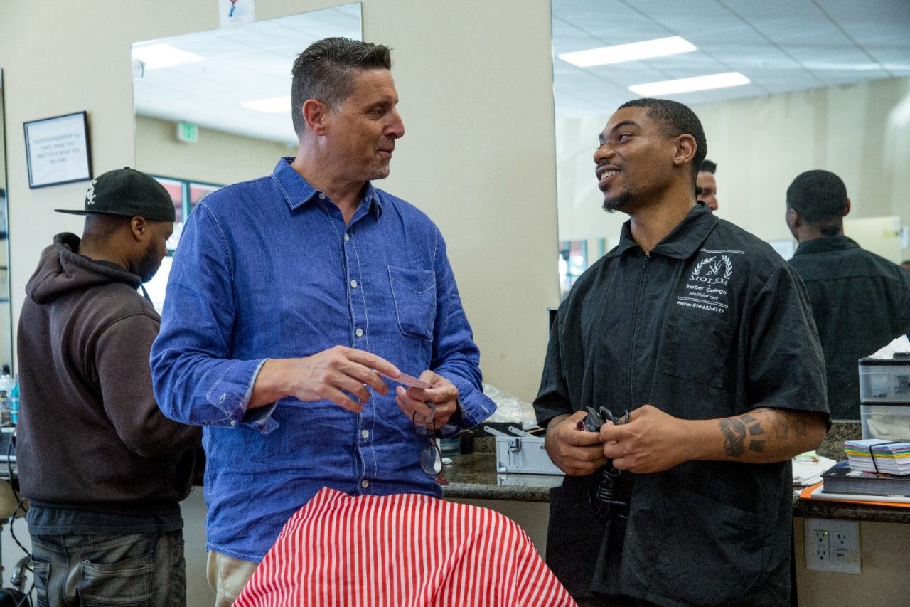 Frank Quattro, owner of Moler Barber College, speaking with Jamon Smallwood, a student. Another student, Menyoli Westbrook, looks on. To get people into jobs that pay a living wage, the San Pablo Economic Development Council partners with groups that teach skills, such as haircutting at the Moler Barber College.