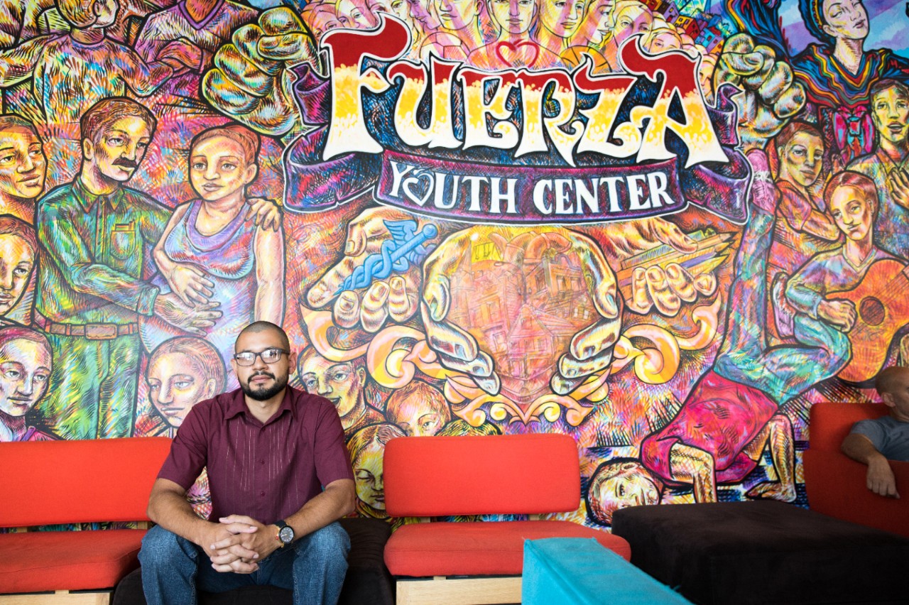Man sitting in front of a youth center wall mural.
