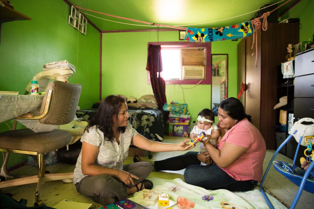 Two women sitting on the floor, playing with an infant.