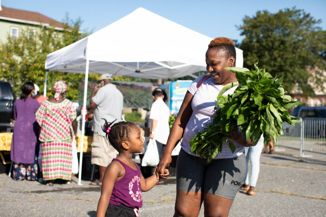 A woman holds her daughter's hand while carrying a plant.