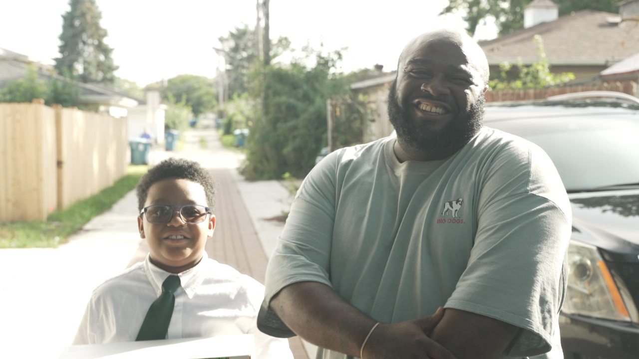 A man and young boy stand together outside smiling. 