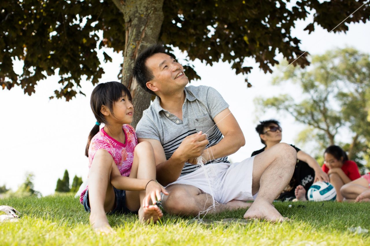 A father and daughter flying a kite in a park.