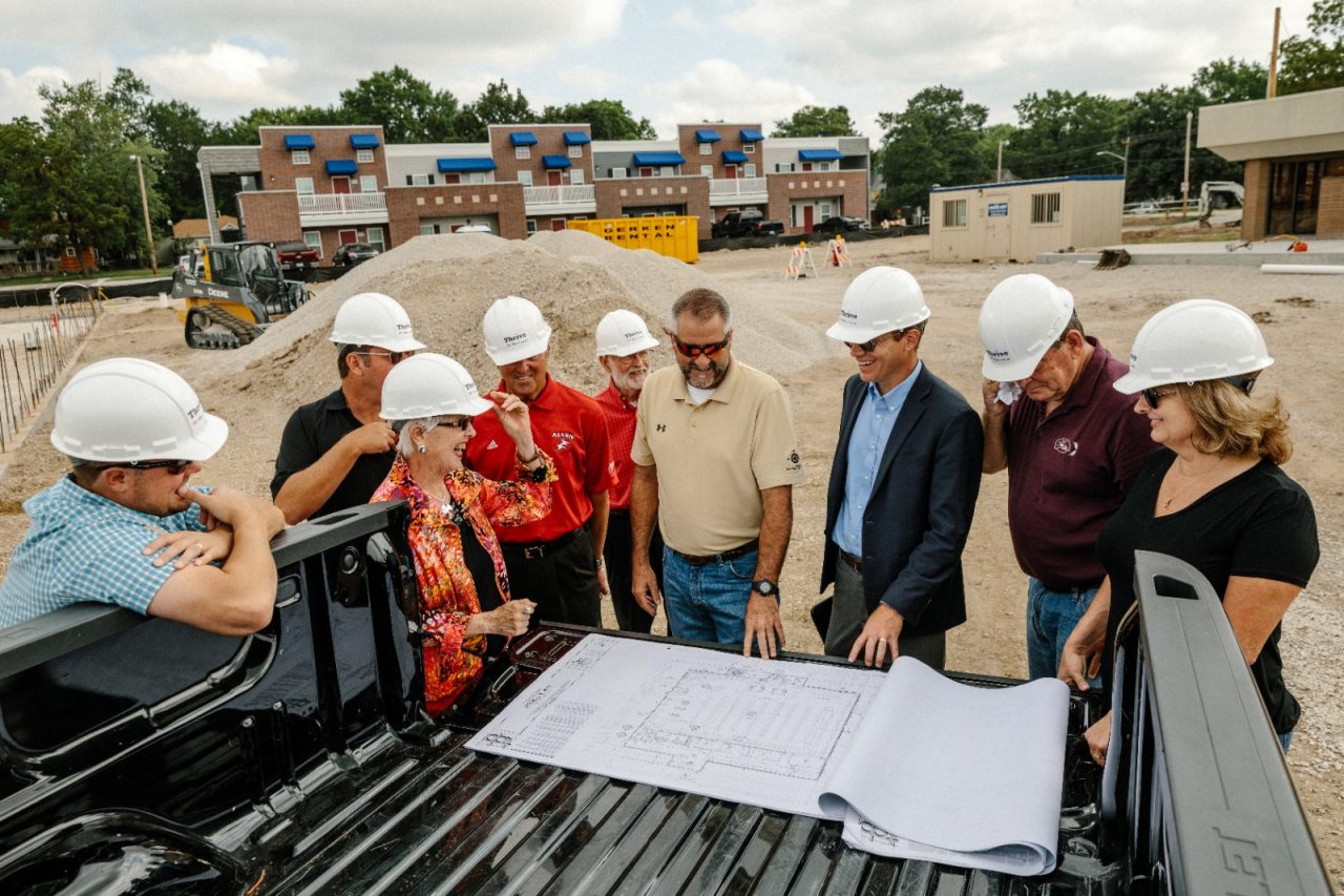 Construction crew and community members review building plans by a pickup truck.