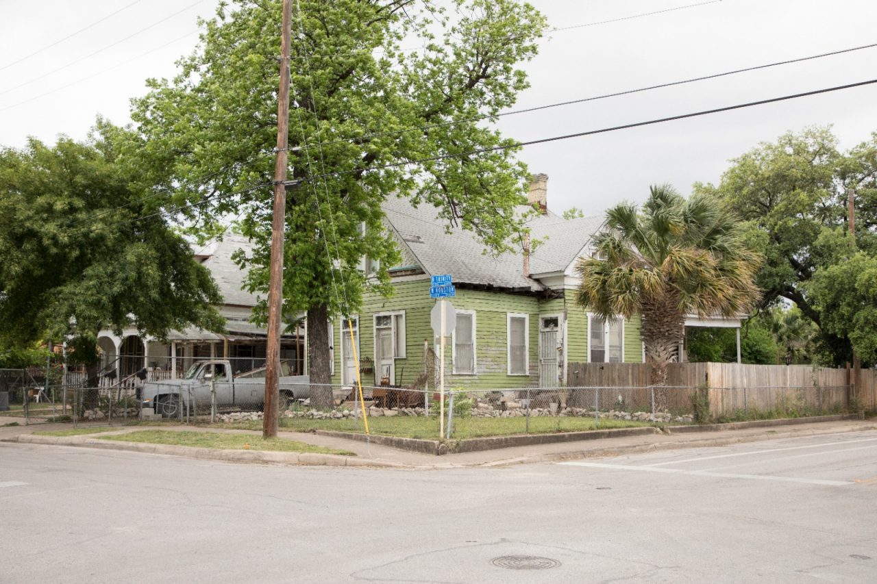 A green, fenced-in house on a street corner.